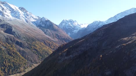 Drone-flight-over-a-lush-green-valley-with-snow-capped-mountains-in-switzerland-in-valais