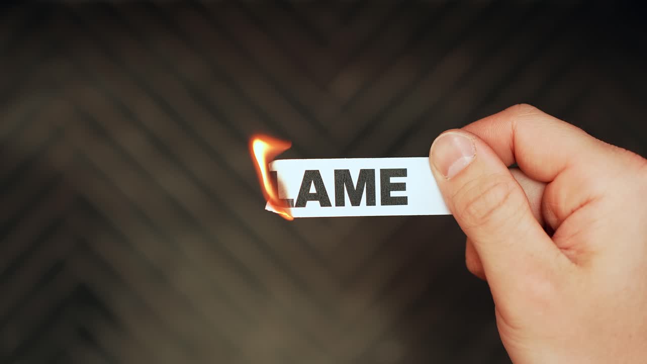 Hånd holder en papirstrimmel med teksten "SKYLD", mens kanten antændes af en lighter – symboliserer ansvarlighed, konflikt og at give slip på en mørk baggrund med plads til tekst.