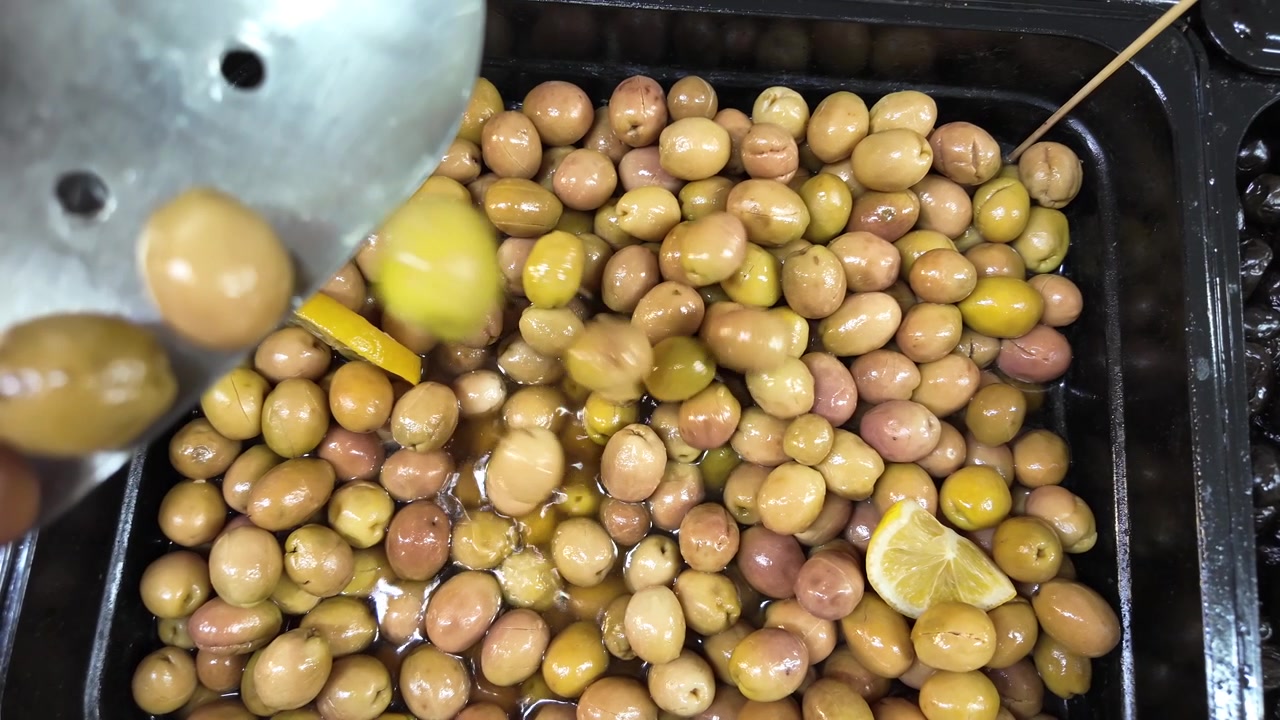 Primo piano di olive verdi versate in un espositore del mercato.
