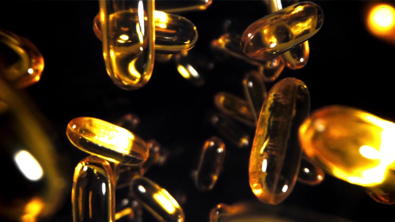 Capsule softgel dorate che fluttuano al rallentatore su sfondo nero