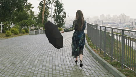 雨の日の市内の公園で傘を持ったポジティブな女性が走っています ⁇