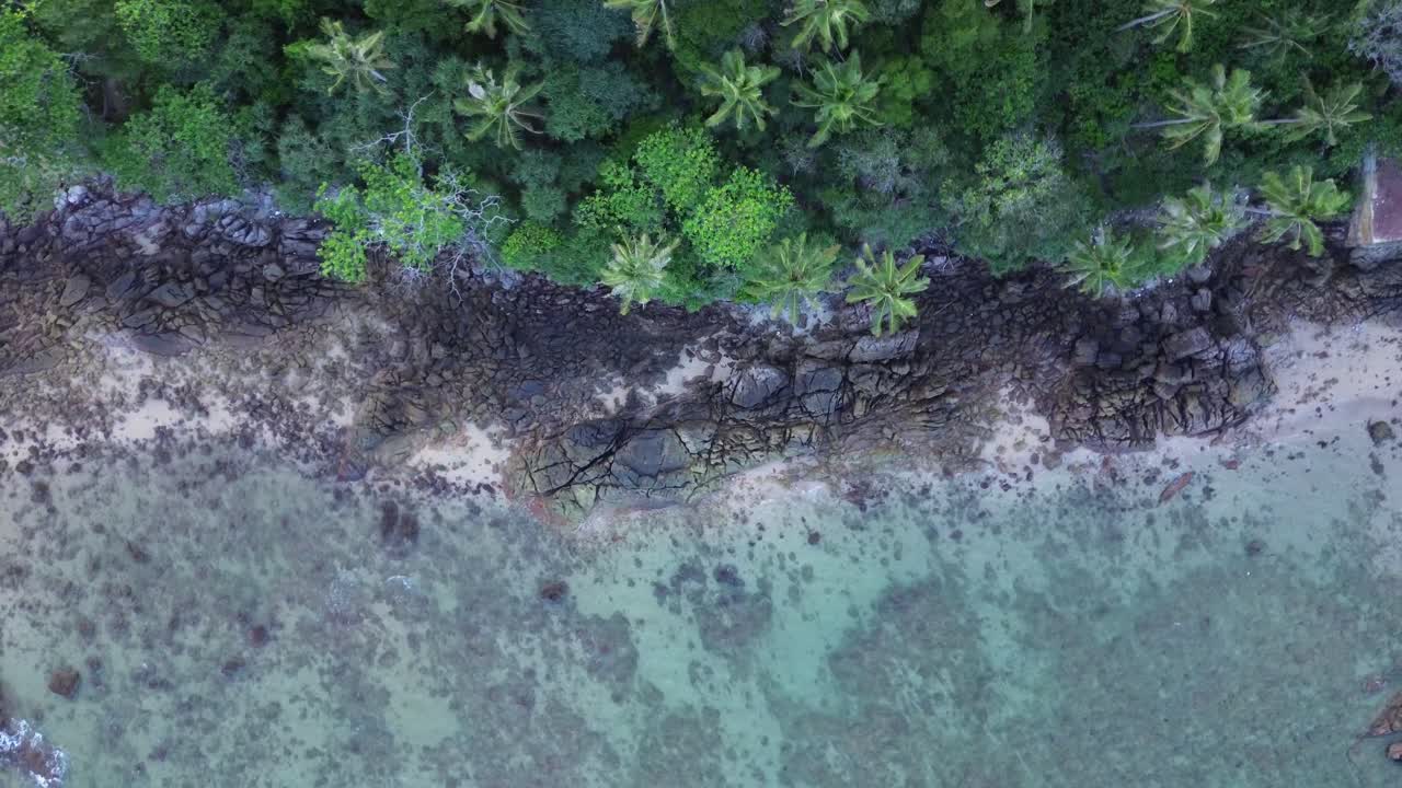 Droneoptagelse i fugleperspektiv af en klippefyldt, tropisk kystlinje på Koh Lanta i Thailand med palmer, en lille sandbugt og turkisgrønt vand langs Andamanhavet. Ingen mennesker, fjerntliggende beliggenhed.