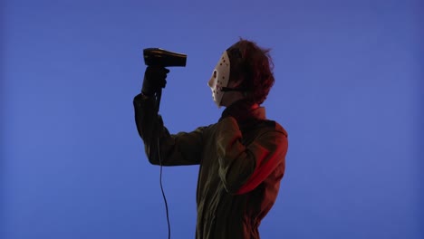 man in white mask drying hair with hair dryer on blue background with red neon light image of maniac - man in white mask drying hair with hair dryer on blue background with red neon light. image of maniac jason voorhees from friday 13. halloween celebration concept