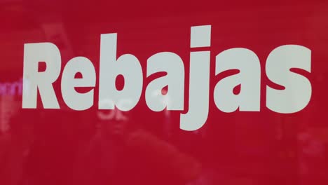 vista de un letrero de una tienda que anuncia el comienzo de la temporada de ventas mientras los peatones se ven relectados en el vidrio de la ventana en el fondo en españa
