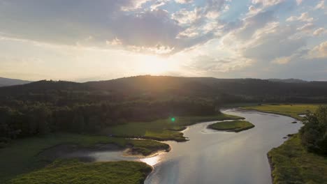 cinematic view from a drone of sunset, when flying over a river that flows through a green countryside in the countryside