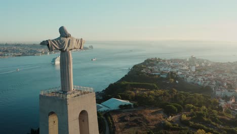 imágenes de drones capturan la estatua de jesucristo en lisboa, portugal, mostrando su tamaño y ubicación en una colina rodeada por la ciudad y la vegetación