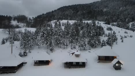 Mountain-wooden-houses-covered-with-snow-with-trees-and-dark-clouds-in-back