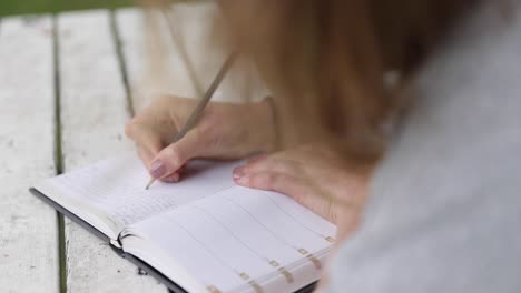 closeup of unrecognizable women writing about her dreams in a journal on a old wooden table in the garden, slow motion