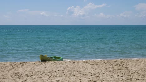 Zeitlupenvideo-Eines-Leeren-Grünen-Kajaks,-Das-Am-Ufer-Eines-Strandes-Mit-Einem-Wunderschönen-Sonnigen-Und-Schimmernden-Meerblick-Am-Horizont-Angedockt-Ist