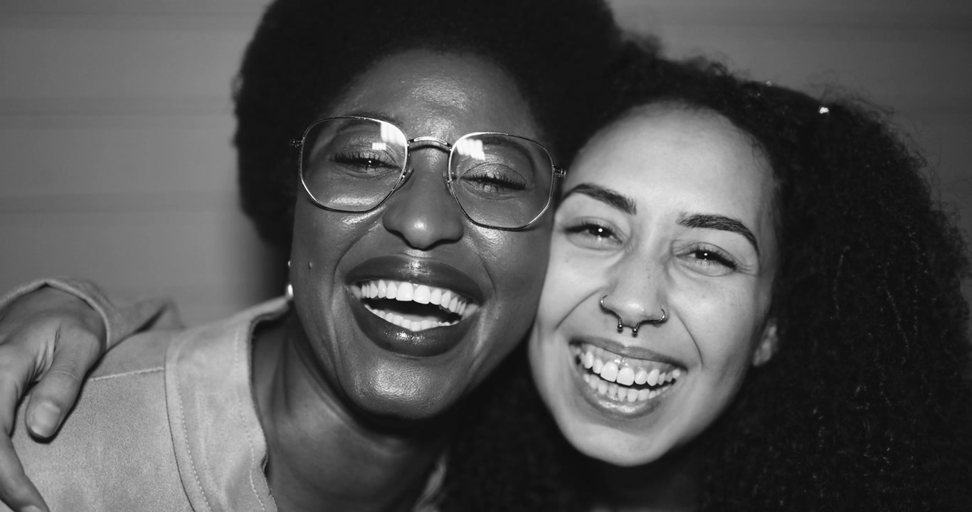 Donne diverse e gioiose che si abbracciano e ridono in bianco e nero