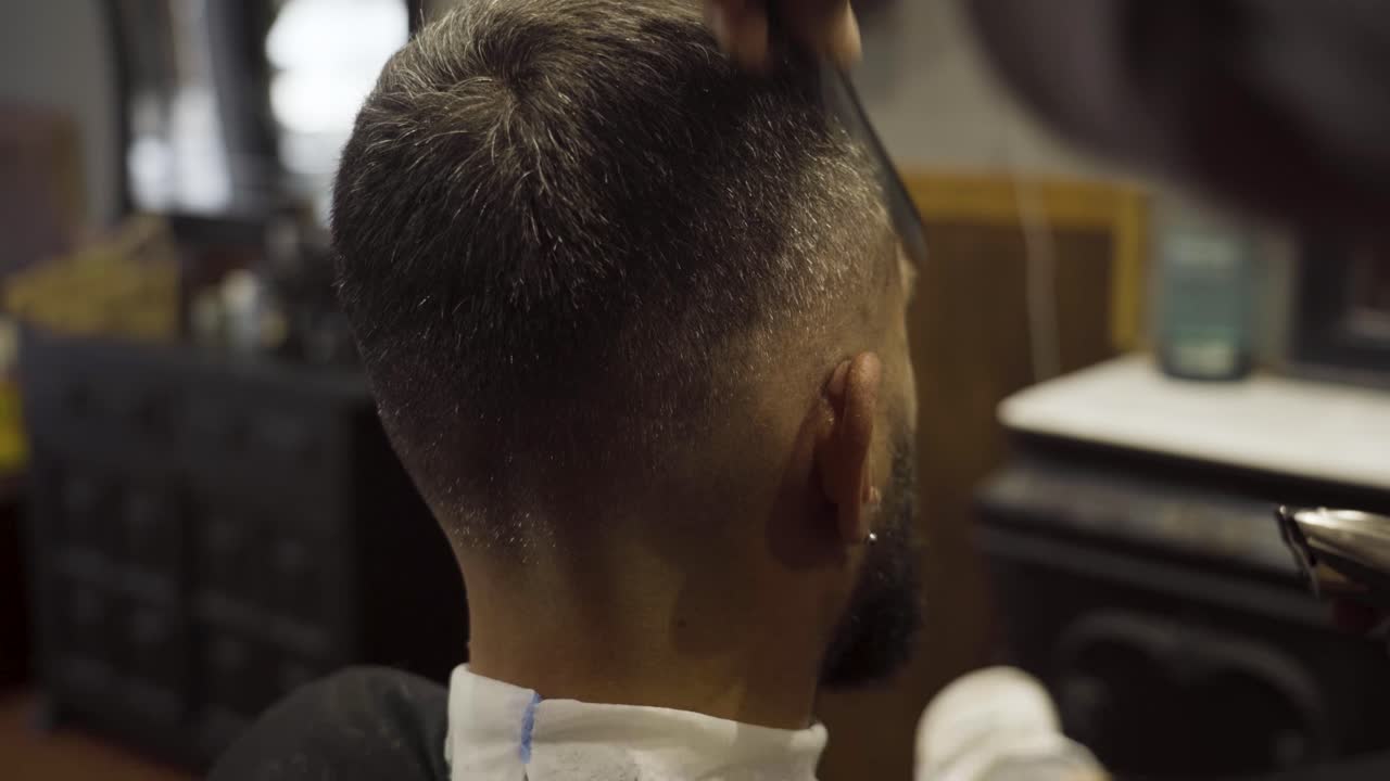 Professionel frisør studser kundens hår med en elektrisk trimmer i en barbersalon