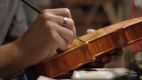 focused luthier varnishing violin in workshop