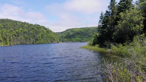 a drone flies quickly forward above a lake with forest-covered mountains in the background with trees on the rights, during the day in northern ontario, canada