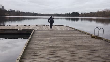 man filming scenery from a wooden dock on a lake with clouds trees sky reflecting off the water