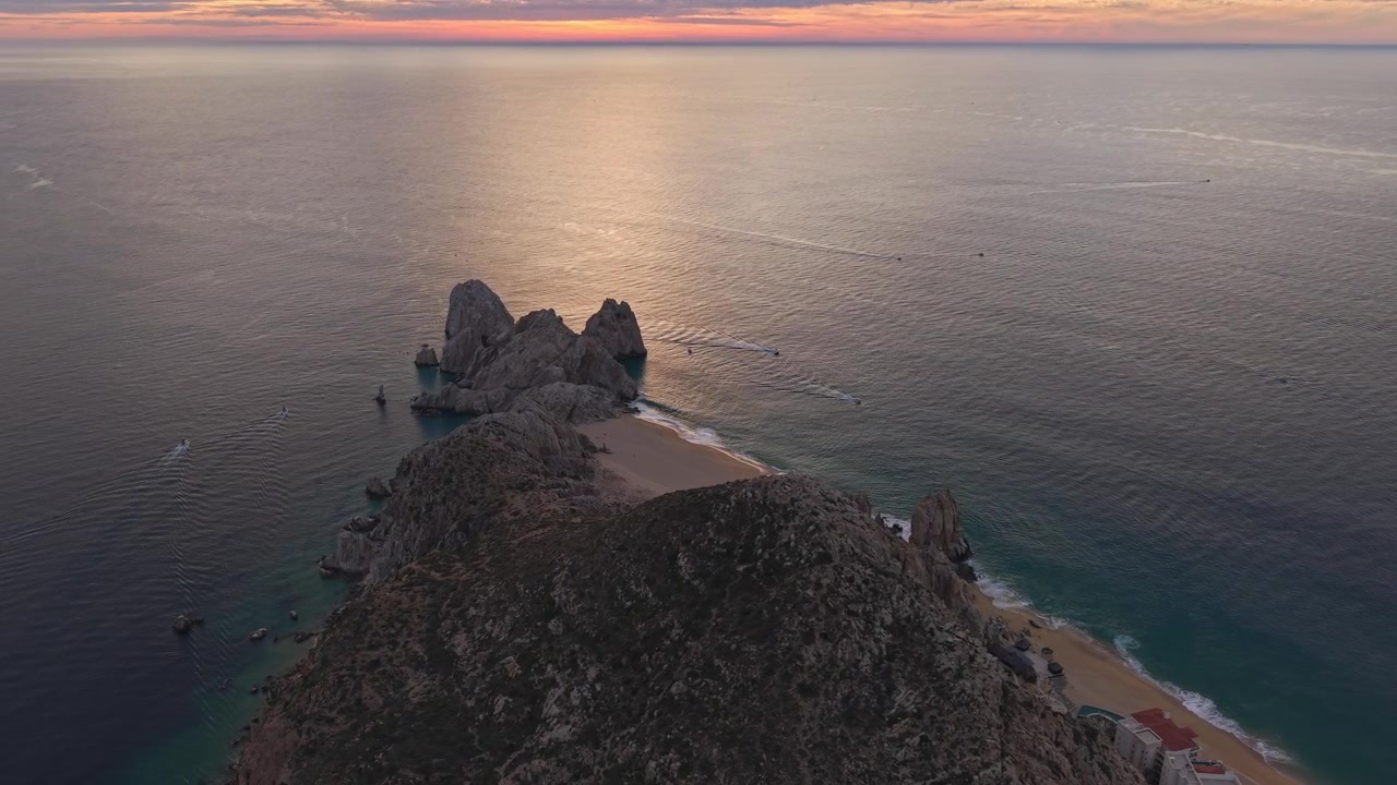 Vista aerea in picchiata verso la Spiaggia degli Amanti a Cabo San Lucas al tramonto, con nuvole arancioni e l'Oceano Pacifico sullo sfondo, Bassa California, Messico