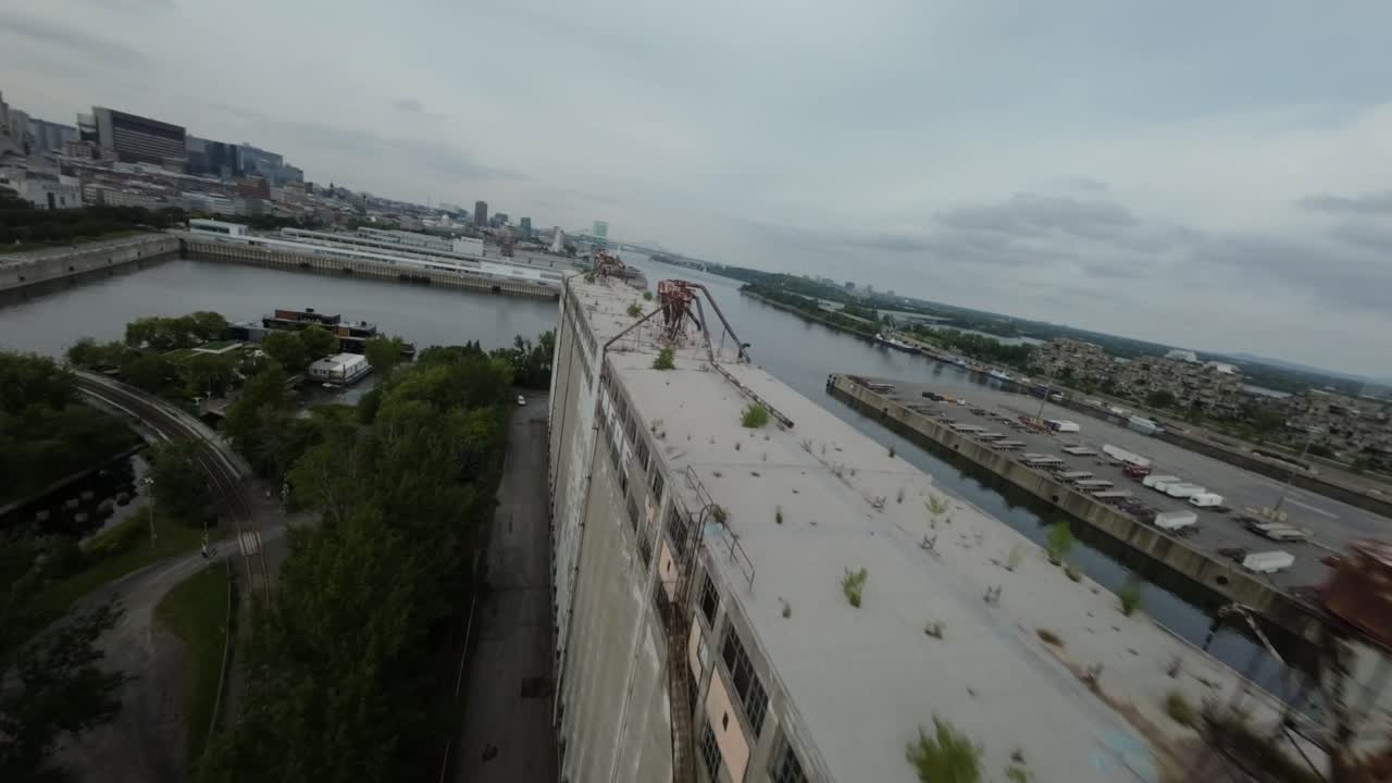 Dynamic FPV drone footage of abandoned Silo 51 at Montreal's old port, industrial structures and the surrounding waterfront cityscape under cloudy skies.