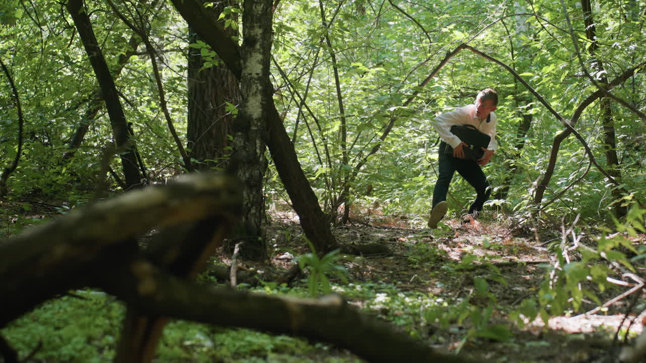Man carrying backpack bending while walking carefully through dense green forest under daylight, navigating branches and trees surrounded by vibrant foliage in natural outdoor wilderness environment