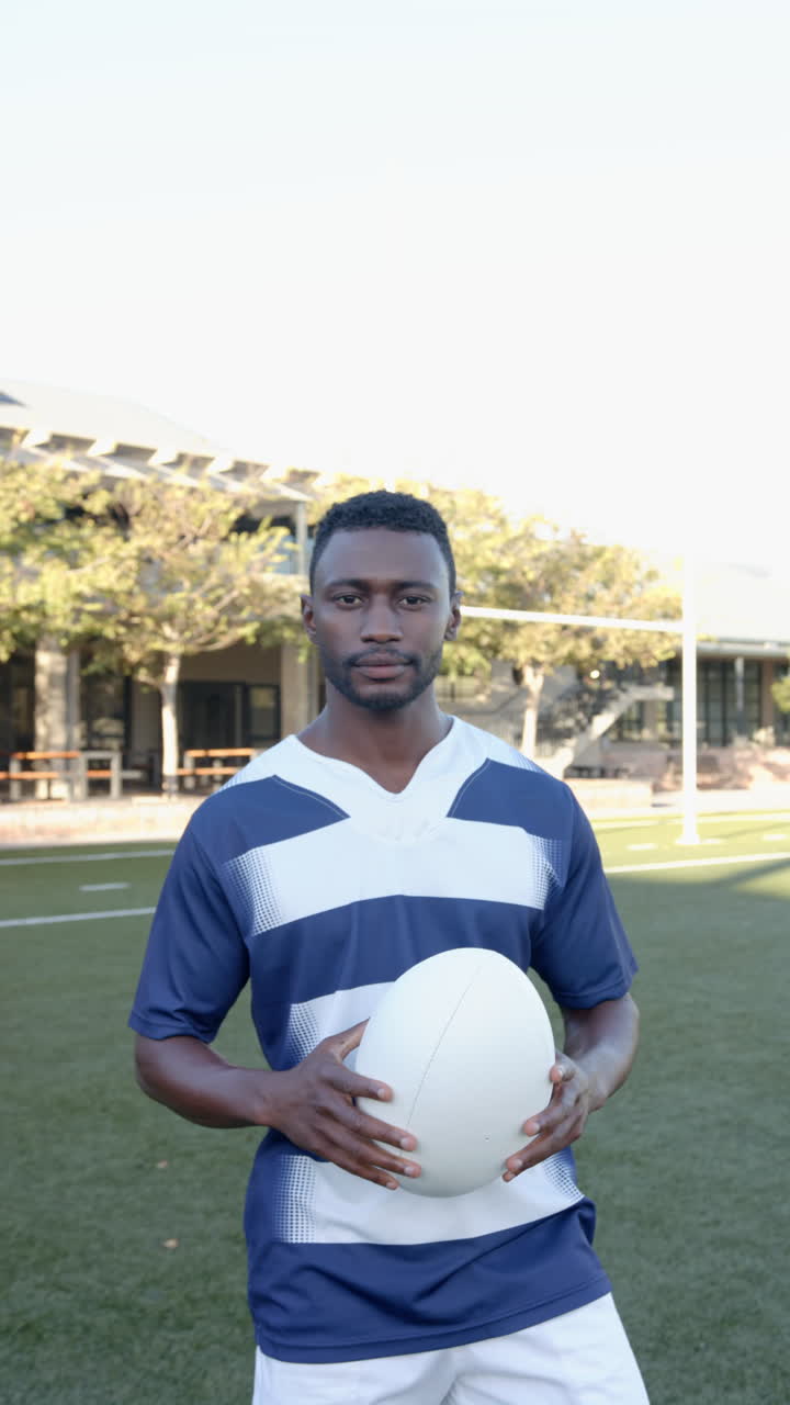 Vertical video: Rugby player holding ball on field, ready for game, focused and determined