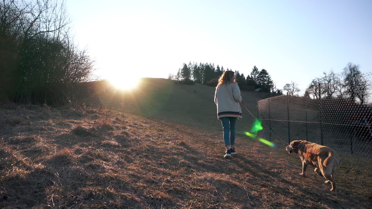 Una giovane donna con il suo cane che cammina su una collina, illuminata dal sole nascente del mattino a Ruzomberok, Slovacchia - Inquadratura medio-ampia