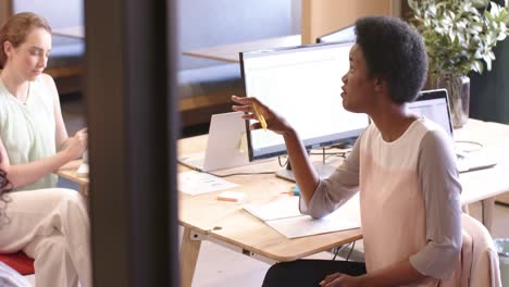 diverse businesswomen sitting at desk and discussing work at office, slow motion