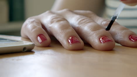 brushing lacquer top coat on red polish fingernails on table, macro