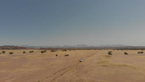 toma panorámica aérea izquierda frente a un vehículo que conduce solo en el desierto a distancia