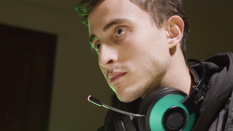 closeup shot of a focused caucasian young man with headphones on his neck sitting at table and working on computer