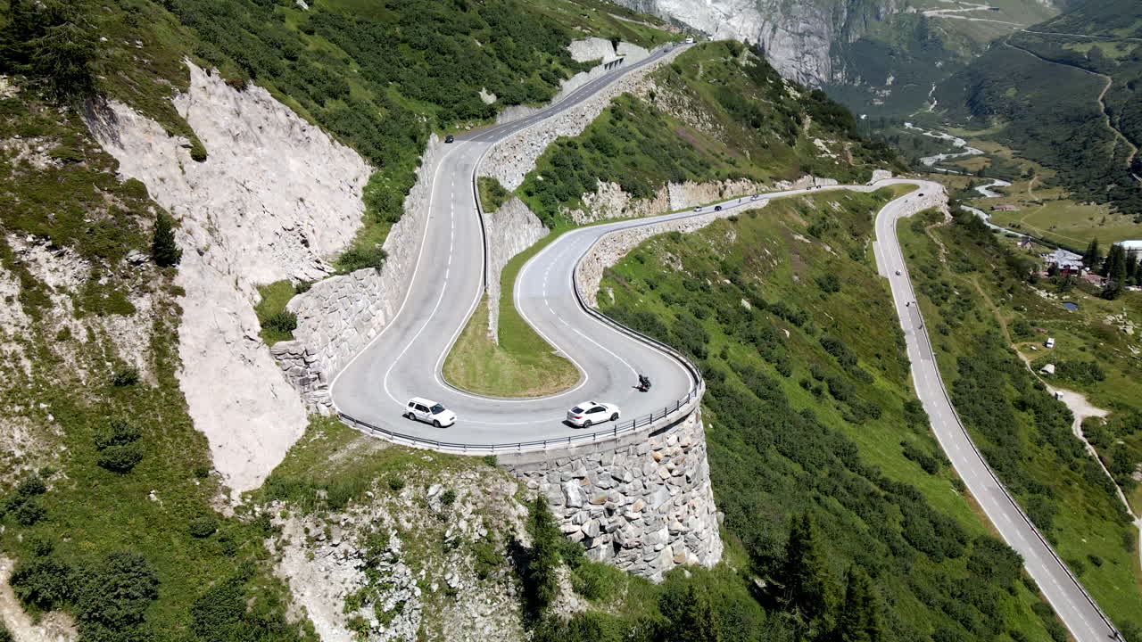 seguimiento de una toma aérea panorámica de dos autos blancos y una moto tomando una curva muy cerrada en grimselpass, suiza