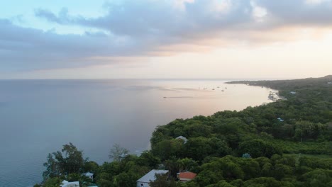 ascending aerial view of caribbean coast with boats, turquoise water, clouds, resorts at sunrise with island background, roatan island,west end, honduras