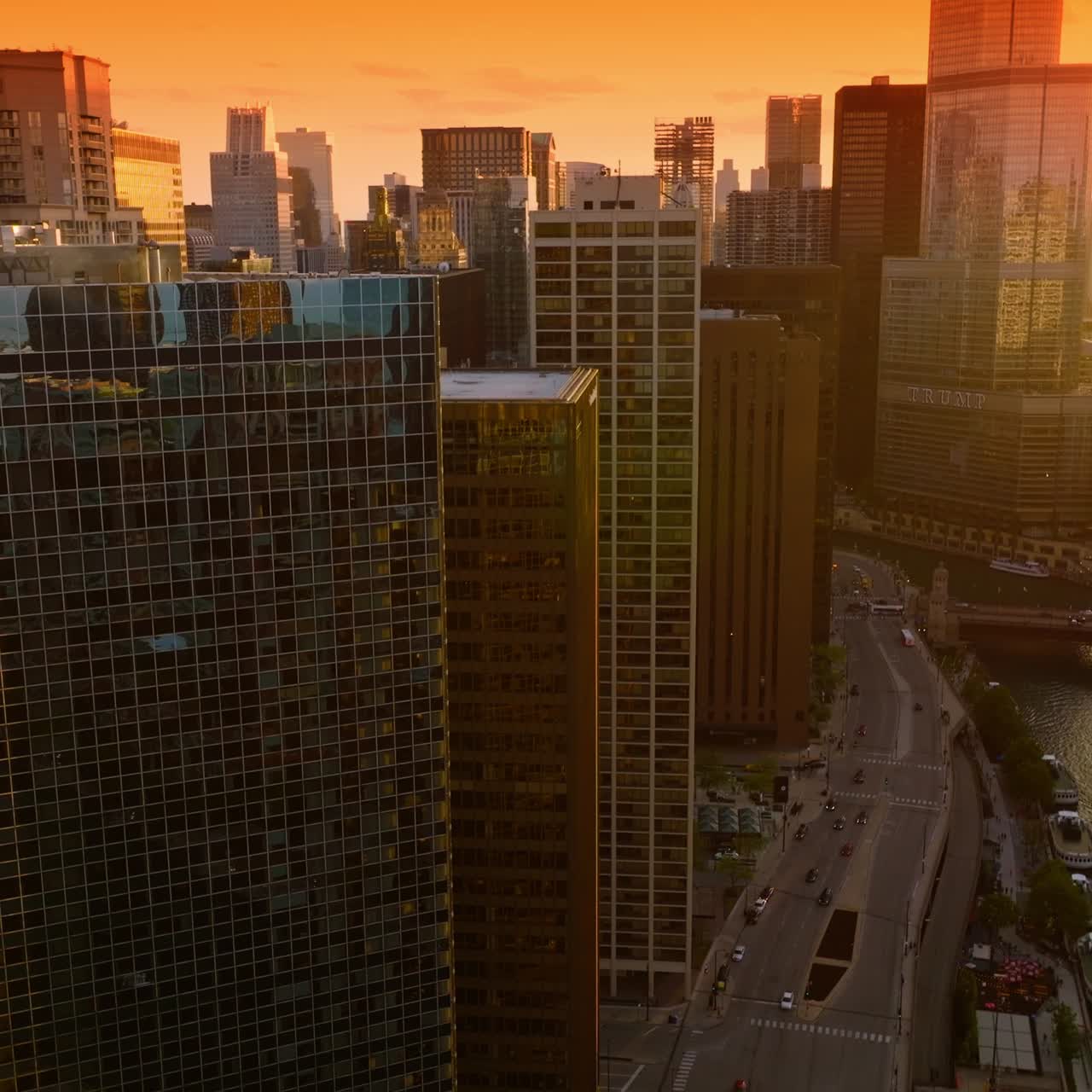 Um belíssimo pôr do sol refletindo nas janelas espelhadas dos arranha-céus. Drone sobrevoando os telhados sobre o Rio Chicago. Céu laranja brilhante ao fundo