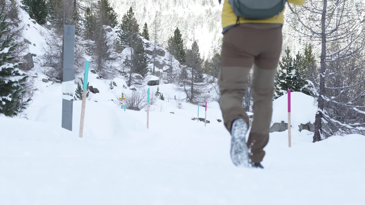 hombre caucásico con una mochila y una chaqueta amarilla caminando por un sendero cubierto de nieve en un bosque