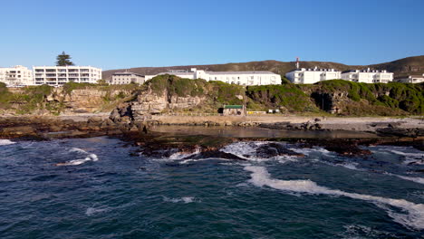 Aerial-over-ocean-with-view-of-marine-tidal-pool-on-jagged-coastline,-Hermanus