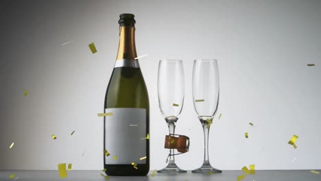 confeti dorado cayendo sobre una botella de champán y dos copas de champán contra un fondo gris