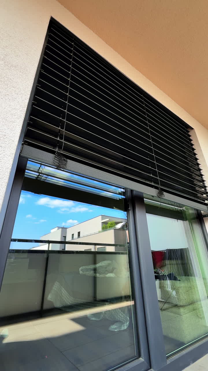 Modern window blinds on a sunny day. Black horizontal blinds cover a large window, letting in sunlight and creating a stylish appearance of the space