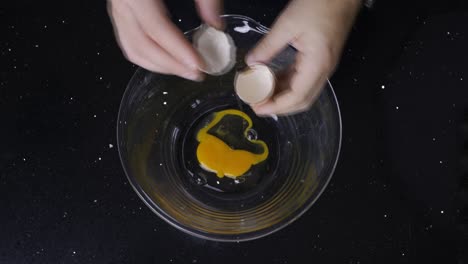 topdown view of cracking fresh eggs into a glass bowl