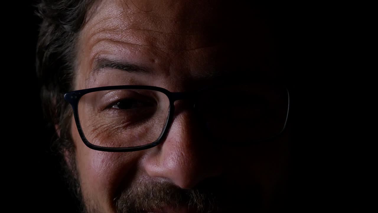 mezza faccia di maschio che ride, mezza età, con gli occhiali, barba, primo piano