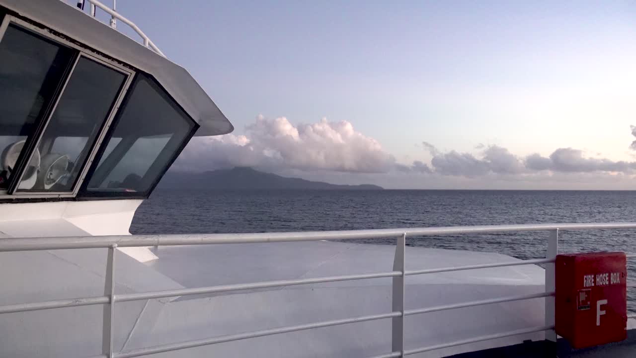 mirando la proa de un barco que viaja a una isla tropical con montañas al amanecer 4k