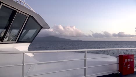 looking-at-the-bow-of-a-ship-traveling-to-a-tropical-island-with-mountains-at-dawn-4k