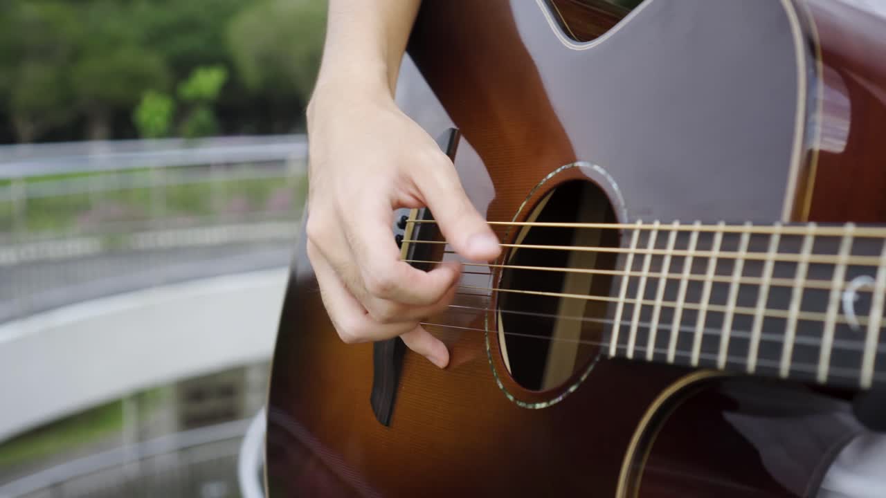 primer plano de un hombre tocando la guitarra marrón y tocando las cuerdas con un fondo escénico