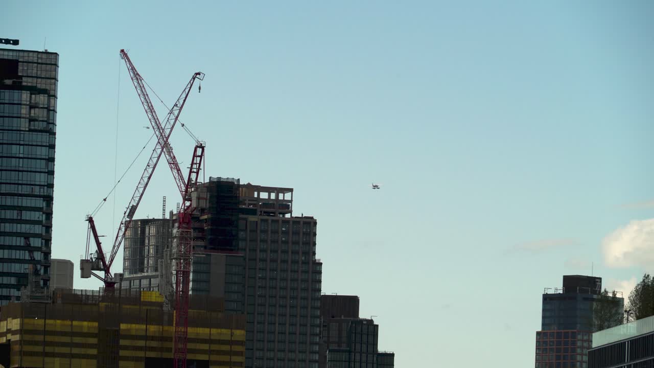 Hidroavión volando con el cielo de fondo, muchos edificios altos en la escena y grúas trabajando en un nuevo edificio residencial