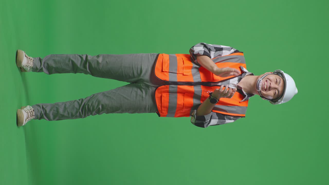 Full Body Of Asian Male Engineer With Safety Helmet Smiling And Clapping His Hands While Standing In The Green Screen Background Studio