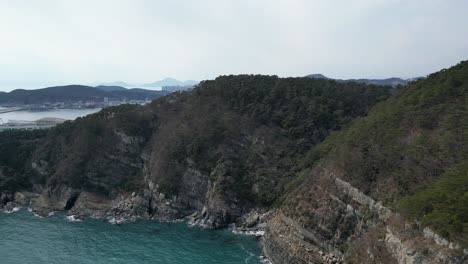 drone aerial view in south korea countryside flying over the clear blue sea of busan next to a green mountain small islands on a sunny day