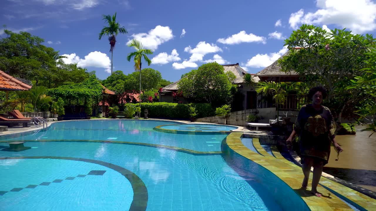 African American woman walking along the pool at the luxury hotel during a bright sunny day. she has a big afro and wears a robe
