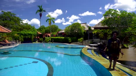 african american woman walking along the pool at the luxury hotel during a bright sunny day. she has a big afro and wears a robe