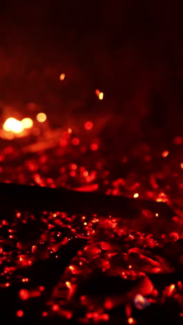 Hot smoldering red embers are moved by the stick. Bright sparkles flying up in the air. Black backdrop. Vertical video