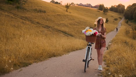 Zeitlupe,-Sexy,-Schöne-Frau-Mit-Einem-Fahrrad,-Einem-Hut-Und-Einem-Leichten-Sommerkleid-Kommt-Mit-Blumen-In-Einem-Korb-Und-Lächelt.