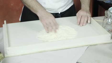 chef pours water from pitcher into flour pile gently mixing with hands to create dough