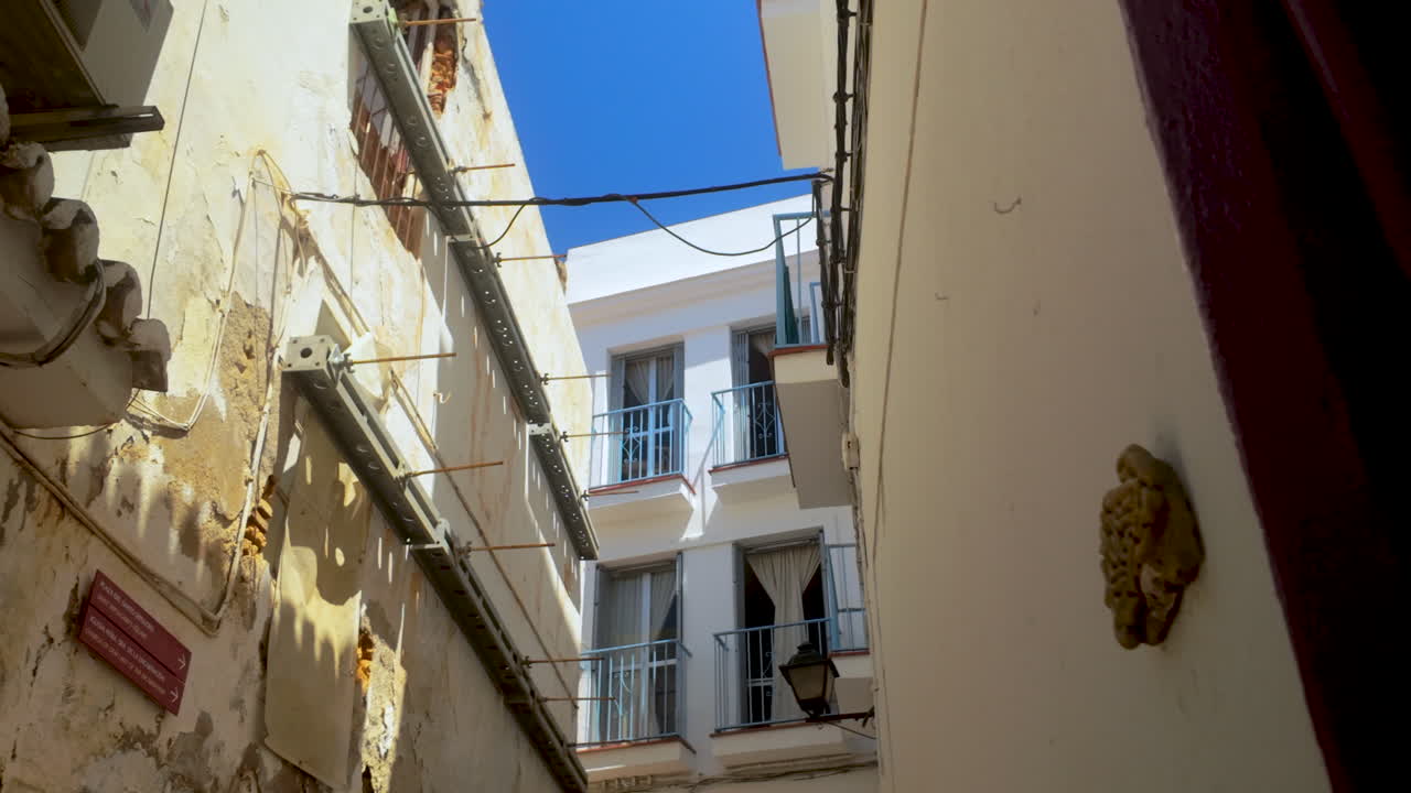 Narrow alley in Marbella, Spain, showing traditional Spanish architecture with white walls, balconies, and a bright blue sky above