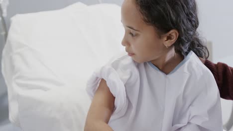 doctor vaccinating biracial sick girl patient with mother in hospital in slow motion