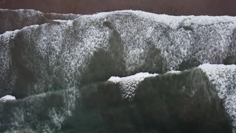 Overhead-drone-shot-of-waves-crashing-onto-a-beach-on-the-Oregon-coast-during-sunset